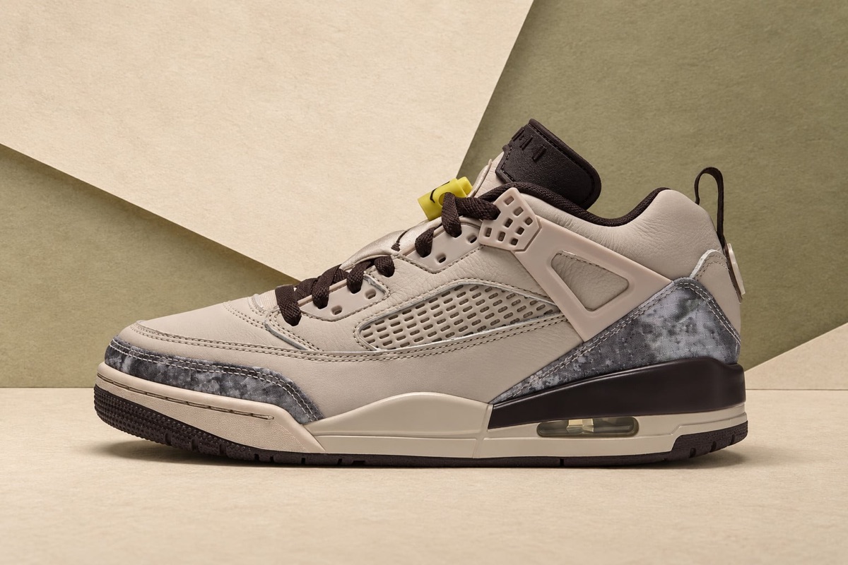 Jordan Spizike Low Realtree Camo de perfil sobre un fondo de planos crema y verde oliva, con upper de cuero crema, paneles de camuflaje gris en la punta y el talón, cordones marrón oscuro y traba de cordones amarilla
