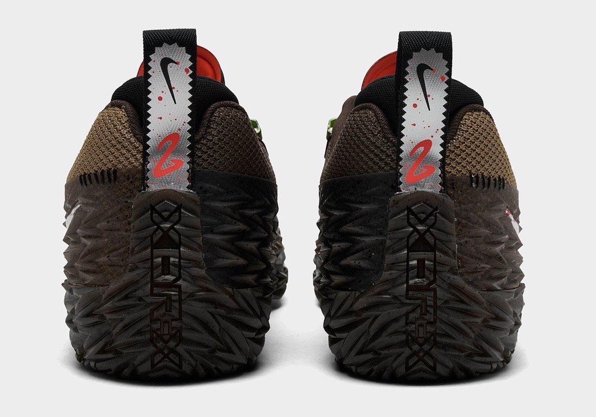 Talones del par de Nike ST Charge Halloween de Cade Cunningham sobre fondo gris claro, con tiradores plateados de borde dentado, el Swoosh negro y el número 2 en rojo rodeado de gotas rojas, y la goma texturada marrón con salpicado negro
