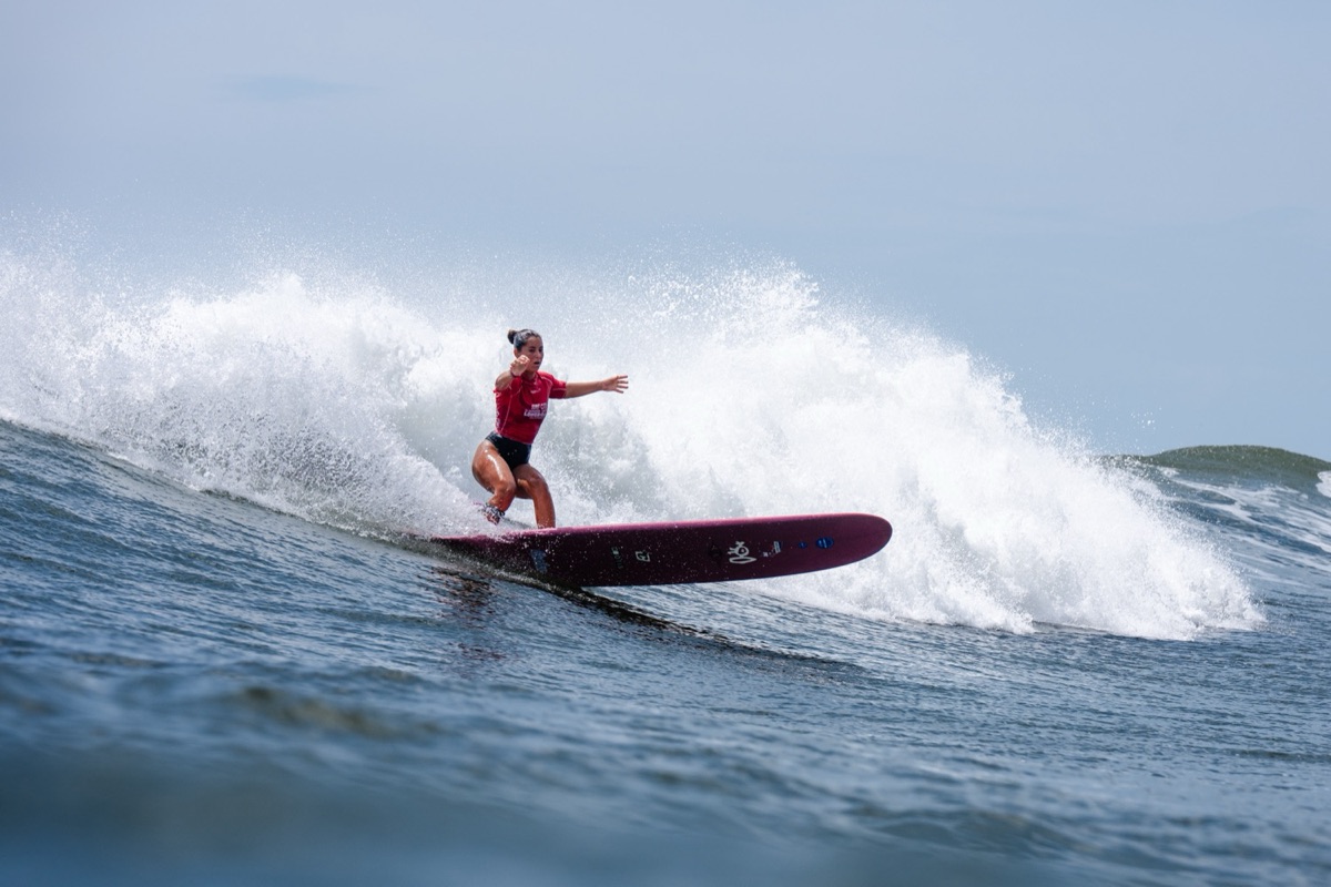 Lia Diaz, con lycra roja, gira con su longboard bordó sobre una ola de El Sunzal con la espuma detrás