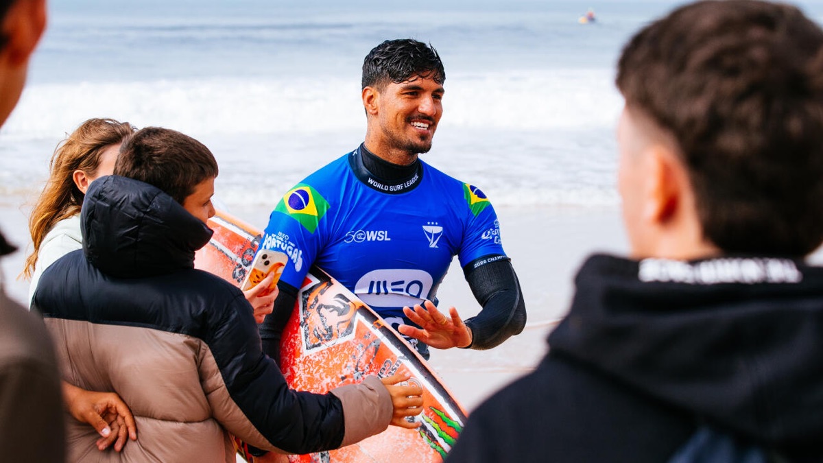 Gabriel Medina, con la lycra azul del MEO Rip Curl Pro Portugal y la bandera de Brasil, sonríe con su tabla naranja mientras lo saludan en la orilla de Supertubos