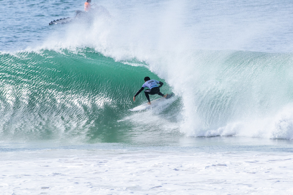 Guilherme Ribeiro, con la lycra blanca, se mete en el tubo de una ola verde en Supertubos durante su serie contra Kanoa Igarashi
