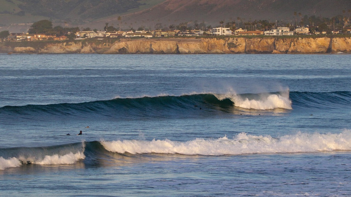 Olas rompiendo frente a los acantilados y las casas de la costa de Pismo Beach, en California, con un surfista remando en el agua