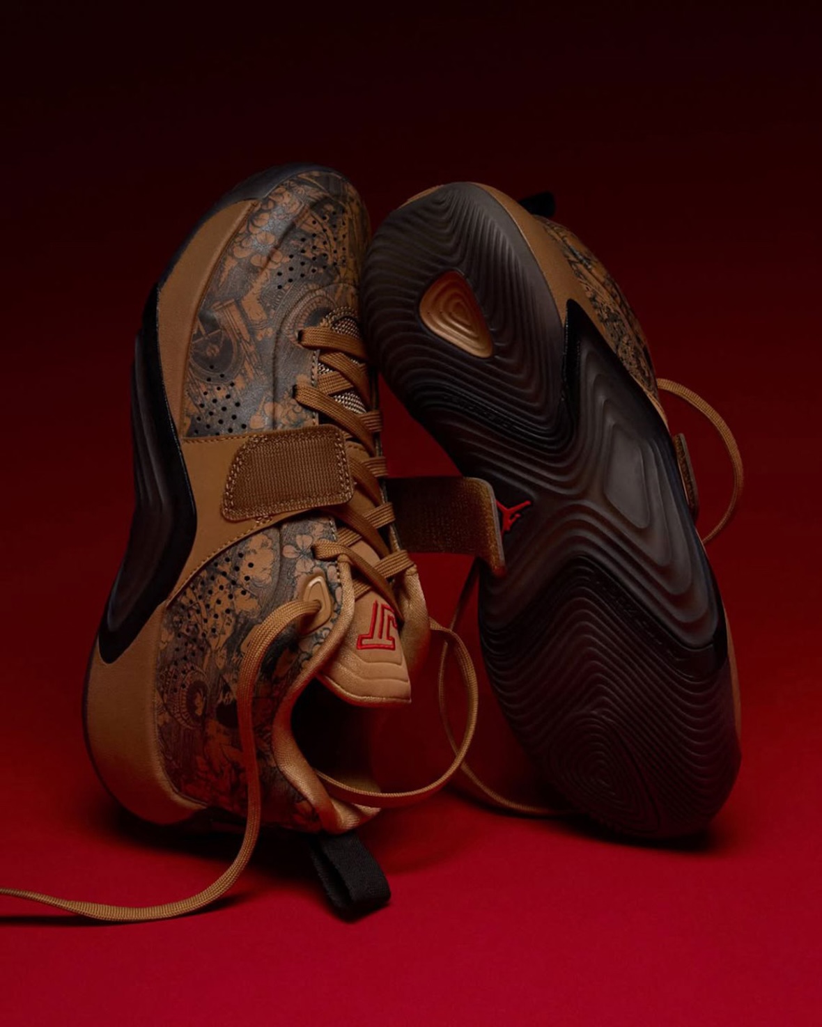 Par del Jordan Tatum 5 Laser parado sobre las puntas, uno de lado con los grabados y el strap, y el otro mostrando la suela marrón oscura con el dibujo de tracción y un Jumpman rojo