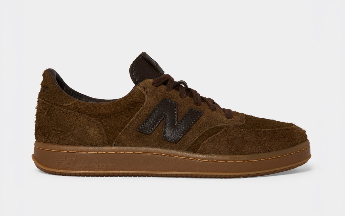 New Balance T500 Espresso de Todd Snyder de perfil sobre fondo gris claro, en gamuza marrón de pelo largo, con la N en cuero marrón oscuro y suela de goma color miel