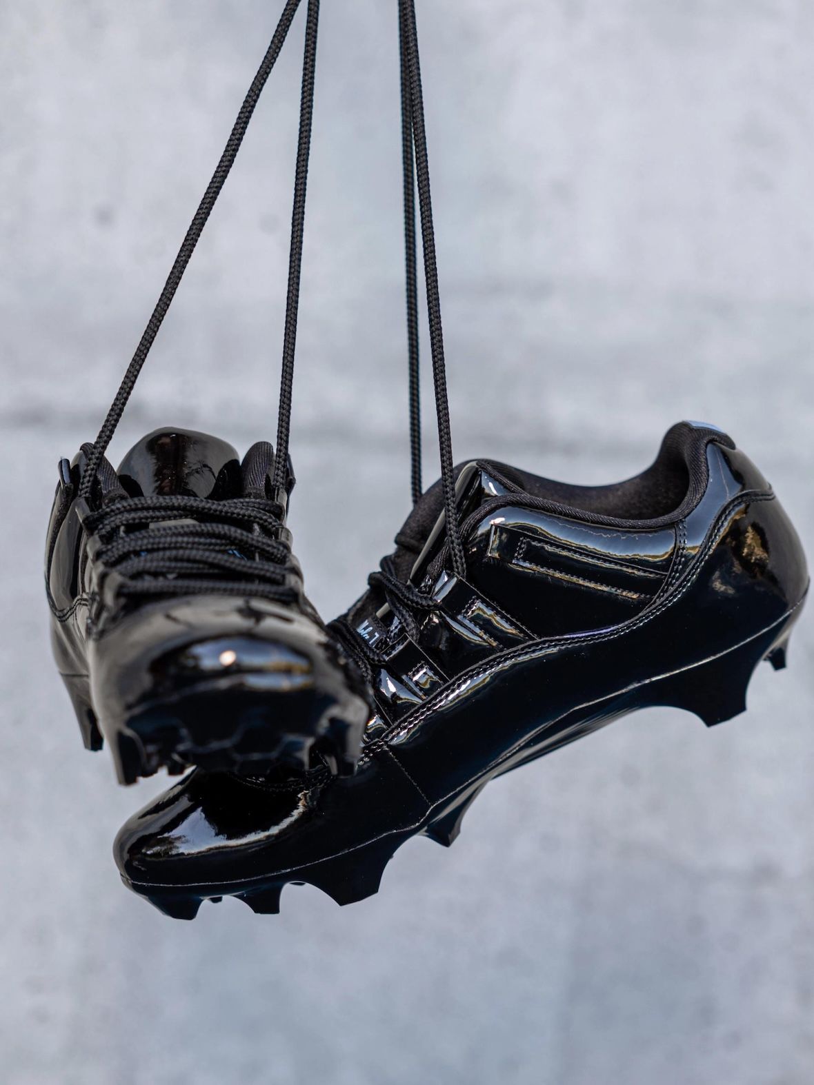 Botines Air Jordan 11 Gammas de UCLA en charol negro colgados de los cordones, con los tapones a la vista