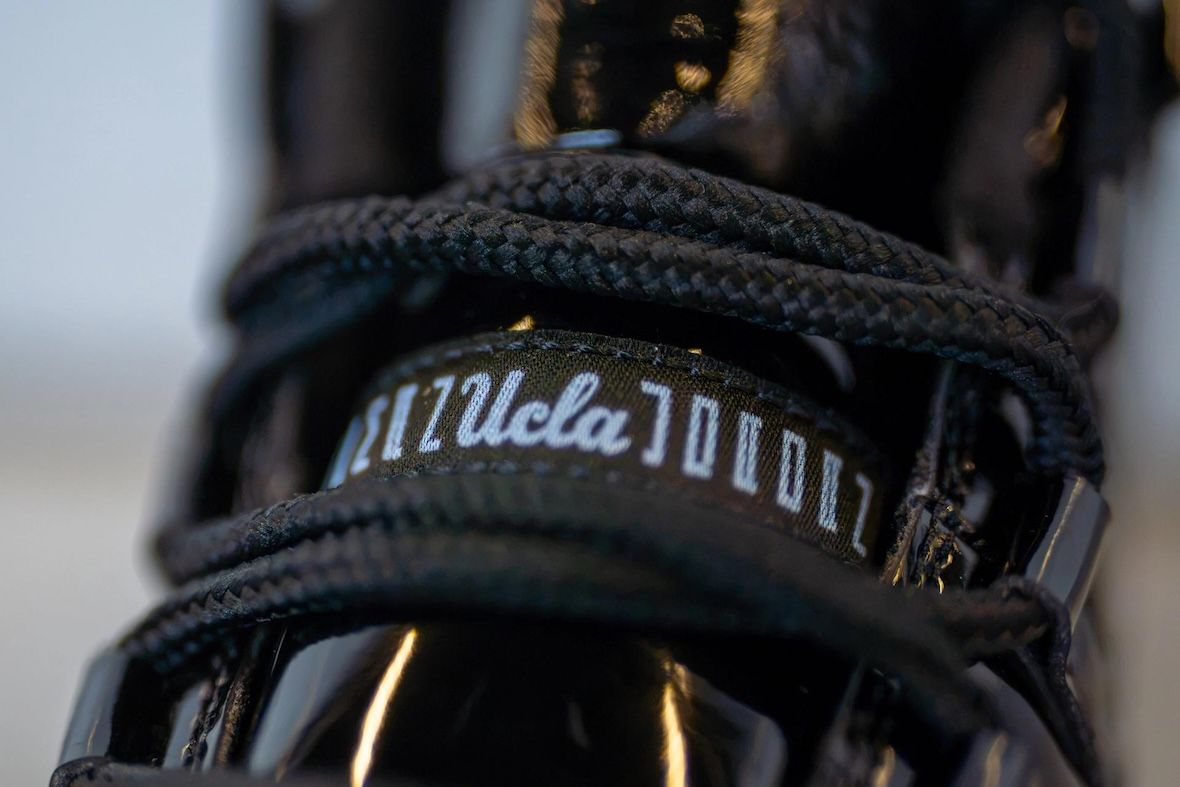 Lengüeta del botín Air Jordan 11 Gammas de UCLA, con el logo de UCLA en letra cursiva repetido sobre una cinta negra