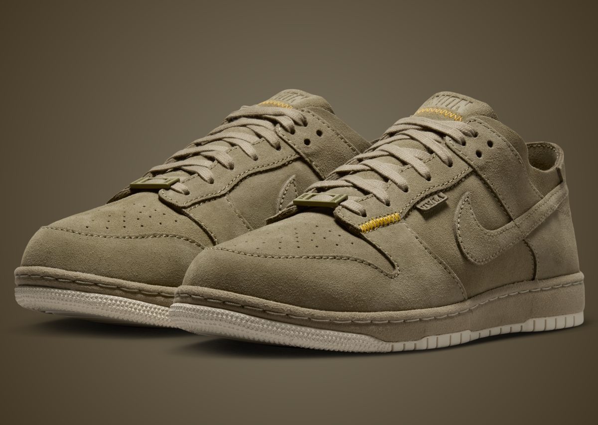 Par de Union x Nike Dunk Low Bamboo en gamuza color bambú, con costuras amarillas en la lengüeta y suela crema, sobre fondo marrón