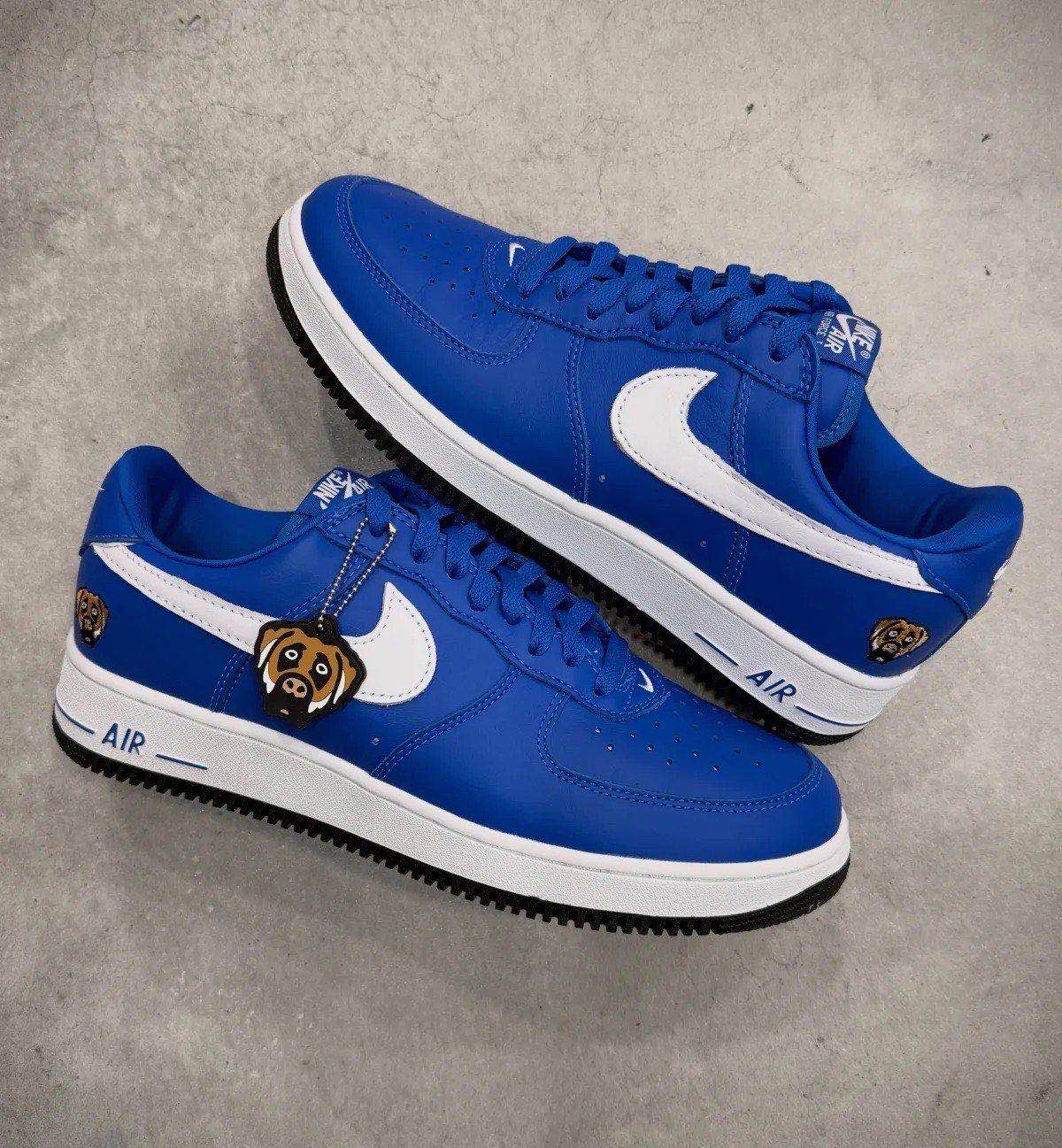Par de Nike Air Force 1 '01 de Victor Victor en azul apoyado sobre un piso de cemento, con el llavero del perro colgando de los cordones